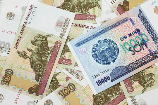 A close up image of a ten thousand Uzbek som bank note on a background of Russian Federation one hundred ruble bills bills in macro