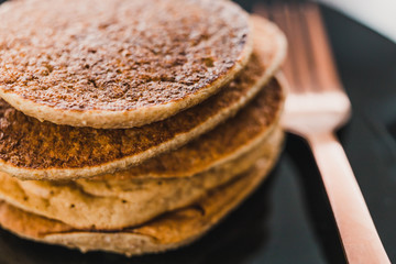 close-up of vegan banana pancakes stack on black plate with copper fork