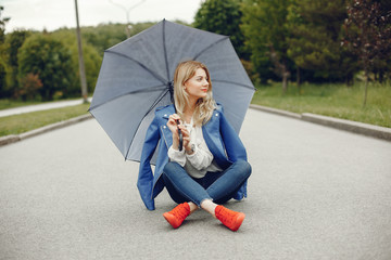 Pretty girl in a summer park. Woman sitting on a asphalt. Lady with blonde hair. Famale with umbrellas