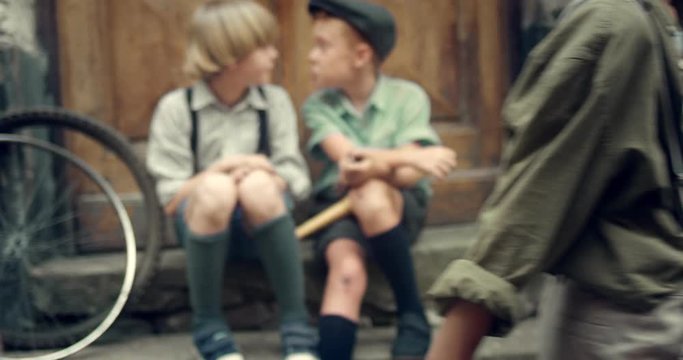 Caucasain little boys in retro style sitting on the steps outdoor and talking while other two boys meeting and shaking hands in front of the camera. Outdoor. Close up.