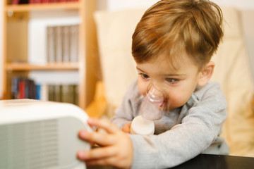 Little small sick boy using steam inhaler nebulizer mask inhalation at home. Medical procedures...