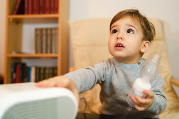 Little small sick boy using steam inhaler nebulizer mask inhalation at home. Medical procedures...