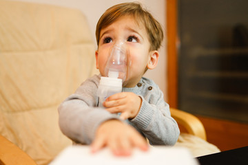 Little small sick boy using steam inhaler nebulizer mask inhalation at home. Medical procedures vapor medication treatment asthma pneumonia bronchitis coughing treatment