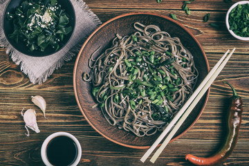 Still life with top view of traditional japanese soba noodles with nori (edible seaweed) and soy sauce, on a wooden surface closeup