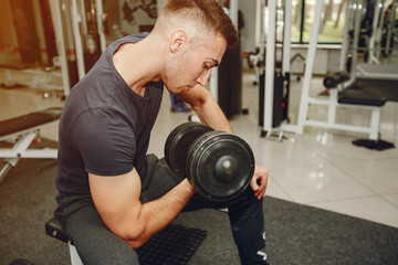 Man in a gym. Guy training with dumbbells. Male in a sportswear