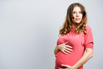 Portrait of surprised beautiful pregnant girl on a gray background. Copy space.