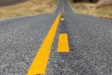 low angle closeup view of yellow dividing and no passing lines and stripes in middle of asphalt road © JJ Gouin