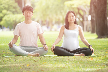 pregnant woman and man are sitting in yoga pose and doing breathing exercise together