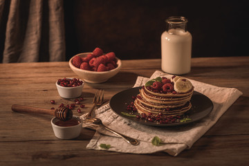 Pancakes with raspberries, banana slices, pomegranate seeds and honey