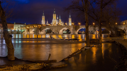 Fototapeta na wymiar Zaragoza - The bridge Puente de Piedra and Basilica del Pilar with the riverside of Ebro river at dusk.