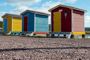 Obraz na płótnie Canvas Red, blue and yellow sheds with colorful doors lined up on a beach with blue sky and clouds in the background.