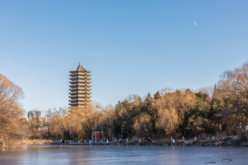 Historical Boya Pagoda or Tower by Frozen Weiming Lake in winter with the moon over blue sky in Peking University, Haidian, Beijing, China.