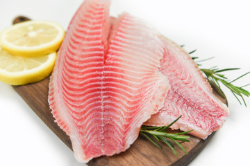 Fresh fish fillet sliced for steak or salad with herbs spices rosemary and lemon - Raw tilapia fillet fish on wooden cutting board and white background and ingredients for cooking food