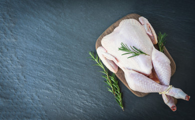rosemary chicken meat wooden cutting board / fresh raw chicken whole on black plate background