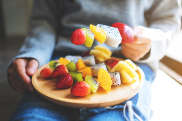 Closeup image of a woman holding a wooden plate of fresh mixed fruits on skewers