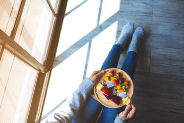 Top view image of a woman eating and holding a wooden plate of fresh mixed fruits on skewers