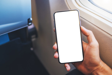 Mockup image of a hand holding a black mobile phone with blank desktop screen next to an airplane...