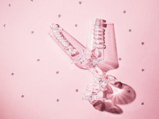 Two champagne glasses with streamers on a pink background with scattered sequins in the harsh light.