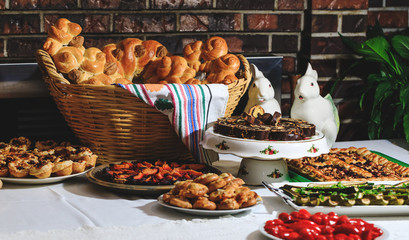 Easter holiday table with traditional bread and authentic Romanian food. Baked buns, colaci or cakes in straw baskets and towel with rustic motifs. Bread in form of snails or pigeons.