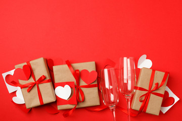 Gift craft boxes with origami paper hearts and wine glasses on red background for Valentines day. Space for text. Seasonal winter february holiday, event flyer concept