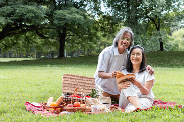 Asian senior couple reading book and picnic at park.