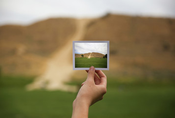 a young girl holding an instant in front of a landscape that is the same but a close up instead of a wide angle