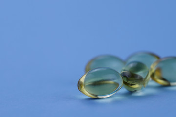 Yellow omega 3 capsules on the right on a blue background. Horizontal, close-up, free space, without people. The concept of medicine and nutritional supplements.