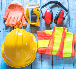 Standard construction safety equipment set including helmet, glasses, glove,  ear defenders and cloth on old blue wooden background. top view, safety first concepts