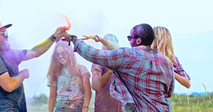 Young African American joyful man jumping and having fun among his mixed-races friends all in paints at the holi festival. Outdoor.