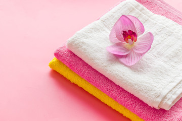 Obraz na płótnie Canvas Clean towels - stack of laundred linen with orchid flower - on pink background copy space