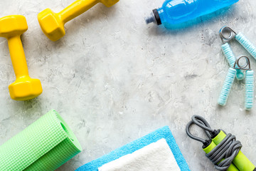 Fitness background - dumbbells, jump rope, sport carpet, water bottle - on grey top-down frame copy space