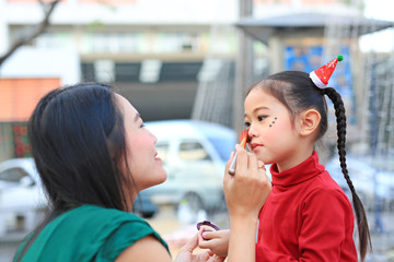 Mother applying makeup on her daughter face.