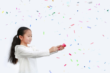 Fototapeta premium Adorable little Asian child girl shooting party popper confetti over white background with copy space.