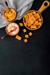 Prepare salted caramel. Scoop with sweet cubes, melted caramel and salt on black background top view copy space