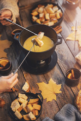 Girl cooks gourmet Swiss fondue dinner with cheese on fire, autumn wooden background with maple...