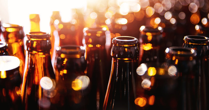 Glass bottles of beer on dark background with sun light. Concept brewery plant production line