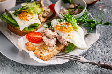 Sea food sandwich. Cod liver, fresh lettuce, pea sprouts, tomatoes and fried eggs. Healty and tasty breakfast on a cutting wooden board. Source of Omega-3 Fatty Acids