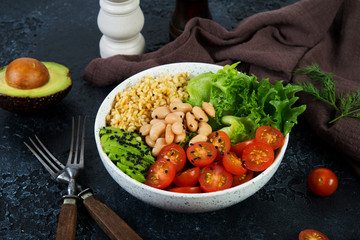 Vegetarian salad bowl on a black concrete background in a plate. Salad of bulgur and fresh vegetables. The concept of clean eating and healthy eating. Horizontal photo.