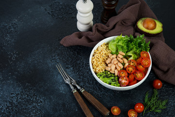 Vegetarian salad bowl on a black concrete background in a plate. Salad of bulgur and fresh vegetables. The concept of clean eating and healthy eating. Horizontal photo with copy space