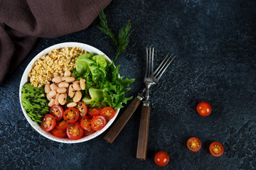 Vegetarian salad bowl on a black concrete background in a plate. Salad of bulgur and fresh vegetables. The concept of clean eating and healthy eating. Horizontal photo with copy space. Top view