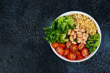 Vegetarian salad bowl on a black concrete background in a plate. Salad of bulgur and fresh vegetables. The concept of clean eating and healthy eating. Horizontal photo with copy space. Top view