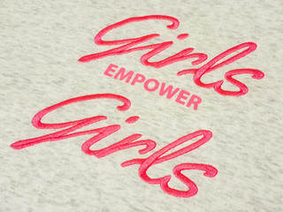 Closeup of pink text girls empower girls quote on grey cotton fabric