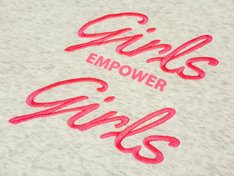 Closeup of pink text girls empower girls quote on grey cotton fabric