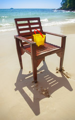 Canned children's toys on a brown wooden chair on the beach on a bright blue day.