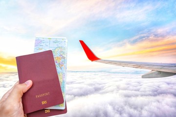 Hand holding passport with a world map and wing of the Airplane flying above the clouds and sunrise sky background.Planning to travel.Traveling Journey Vacation Holiday concept.