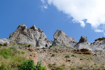 Nature background. Rocks against a bright blue sky and a fluffy white cloud