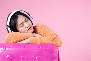Asian using headphone sleeping on luggage with pink background.