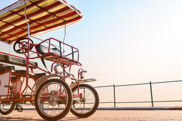 four-wheeled red bike for rent with an awning and a wheel stands on the promenade against the sun. Eco-friendly street transport.