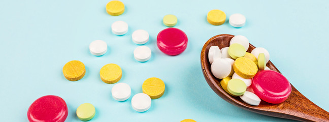 Colorful pills in wooden spoon on a pastel blue background. Flat lay, top view, overhead, mockup, template. Pharmacy and medical concept