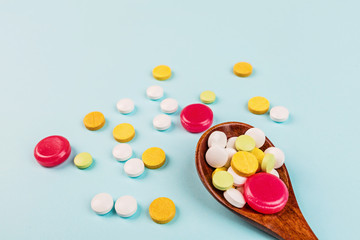 Colorful pills in wooden spoon on a pastel blue background. Flat lay, top view, overhead, mockup, template. Pharmacy and medical concept